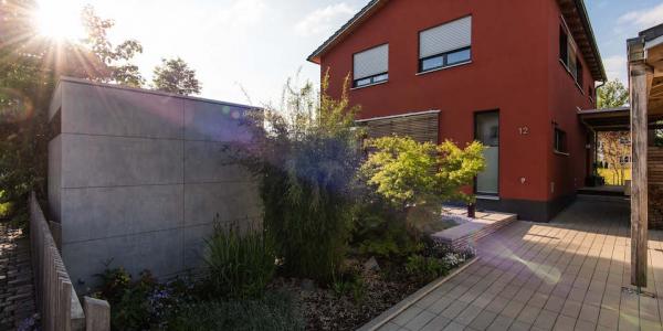 Gartenhaus in Sichtbeton Optik vor rotem Haus