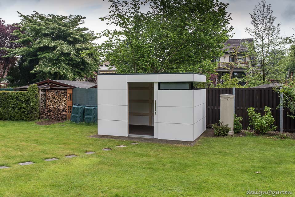 Contrastes en el jardín: la caseta de jardín con techo plano de HPL se combina con el encanto de las casas de campo.