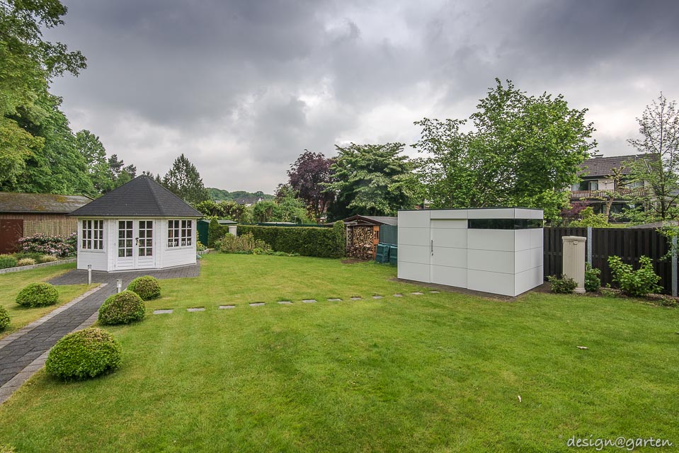 Contrastes en el jardín: la caseta de jardín con techo plano de HPL se combina con el encanto de las casas de campo.
