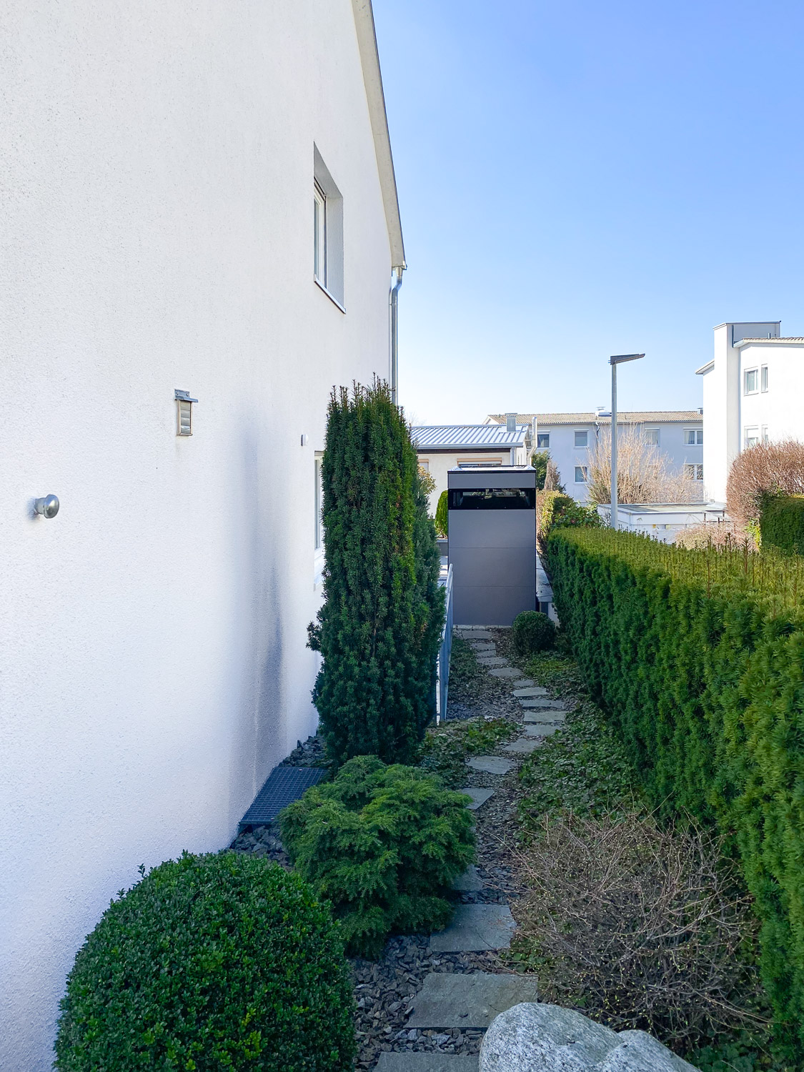 Gepflasterter Weg mit grauem Gartenhaus am Ende